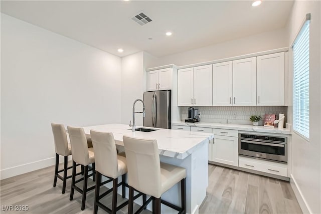 5321 Brayden Ct, Las Vegas, NV 89131 - kitchen featuring appliances with stainless steel finishes, a sink, a center island with sink, tasteful backsplash, and white cabinetry