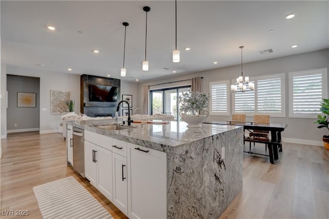 kitchen featuring a sink, light stone counters, light wood-type flooring, stainless steel dishwasher, and baseboards