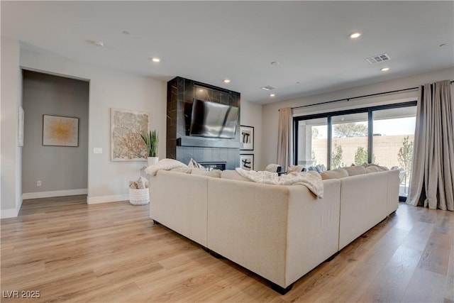 living area with baseboards, light wood-style flooring, a tile fireplace, and recessed lighting