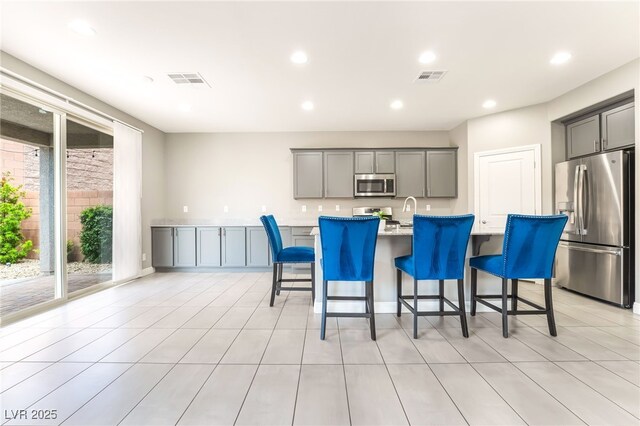 5981 Smith Valley Rd, Las Vegas, NV 89148 - kitchen featuring appliances with stainless steel finishes, gray cabinetry, a breakfast bar area, light countertops, and a kitchen island with sink
