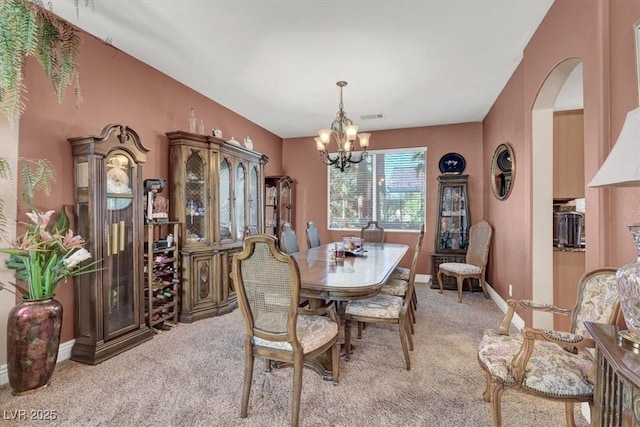 dining area featuring carpet, a chandelier, arched walkways, and baseboards