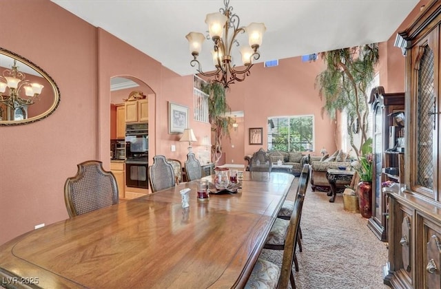 dining area with a chandelier, arched walkways, carpet, and a towering ceiling
