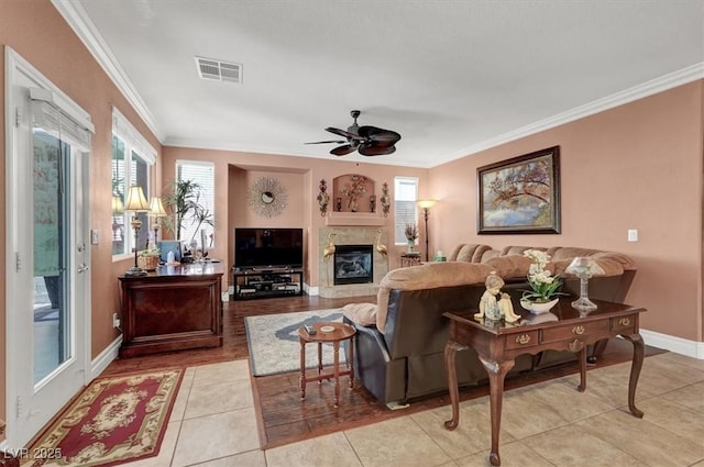 living area featuring ornamental molding, ceiling fan, a premium fireplace, baseboards, and light tile patterned flooring
