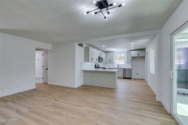 212 View Dr, Las Vegas, NV 89107 - kitchen featuring stainless steel appliances, a peninsula, light wood-type flooring, a textured ceiling, and light countertops