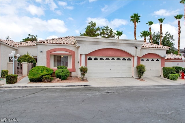 mediterranean / spanish house featuring a tile roof, a garage, stucco siding, and driveway