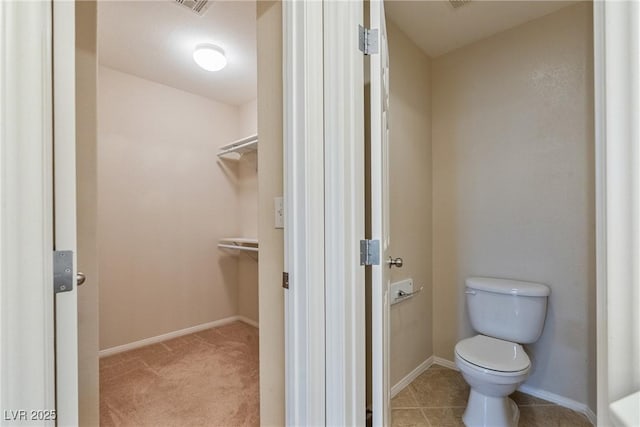 bathroom with toilet, a walk in closet, and baseboards