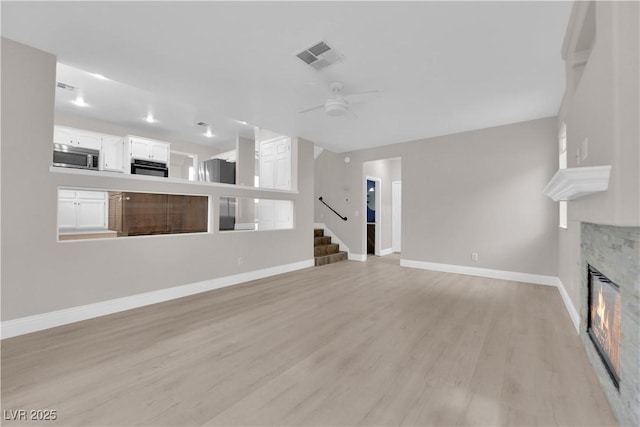 2257 Norway Pine Ct, Las Vegas, NV 89134 - unfurnished living room featuring baseboards, a glass covered fireplace, light wood-style flooring, a ceiling fan, and stairway