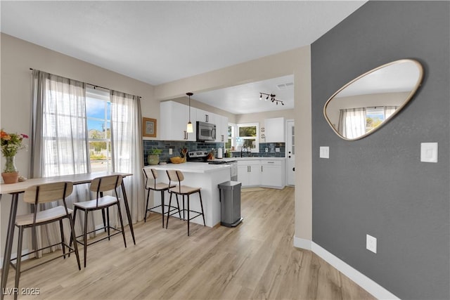 1320 Wengert Ave, Las Vegas, NV 89104 - kitchen with stainless steel appliances, a peninsula, white cabinetry, backsplash, and light wood-style floors