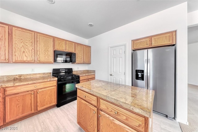 kitchen featuring black appliances, tile countertops, a kitchen island, and light wood-style floors