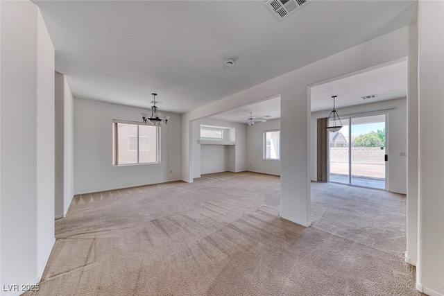 unfurnished living room featuring light carpet, a chandelier, ceiling fan, and baseboards