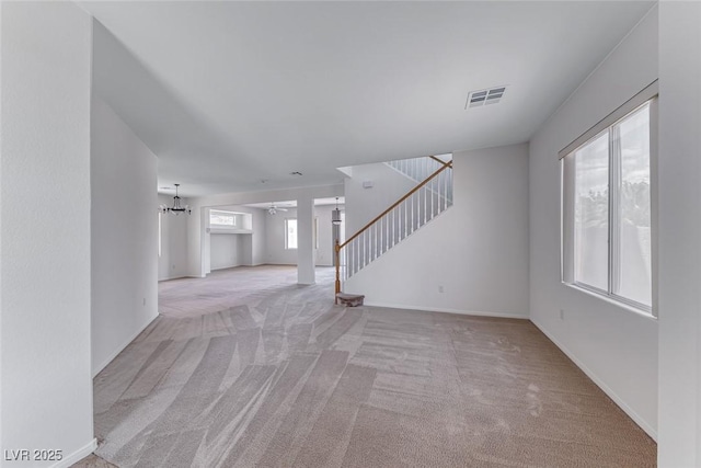 unfurnished living room with light carpet, stairway, a chandelier, and baseboards