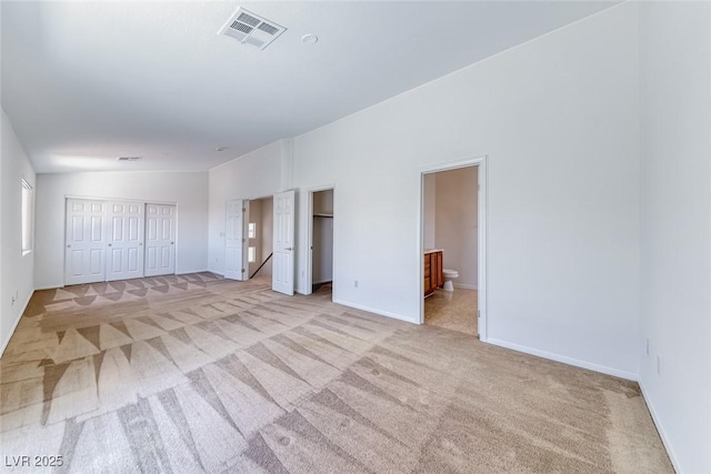 unfurnished bedroom with light colored carpet, two closets, baseboards, and ensuite bath