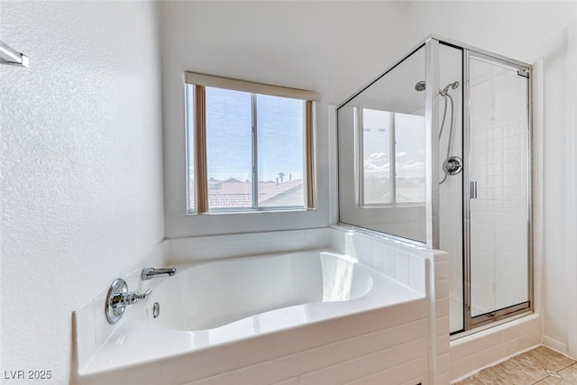 bathroom with a shower stall, a bath, and a textured wall