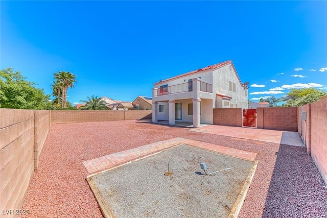 back of house featuring a balcony, a patio area, a fenced backyard, and stucco siding