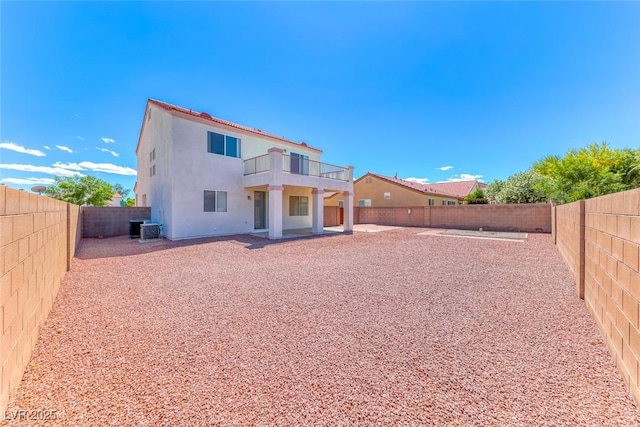 rear view of property with a balcony, central AC unit, a fenced backyard, and stucco siding