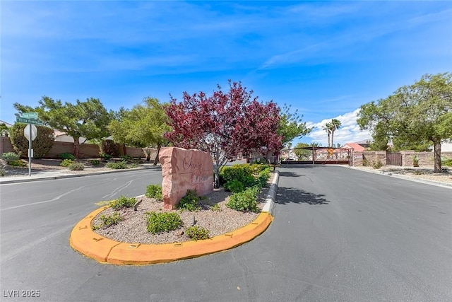 view of asphalt road featuring curbs, a gate, sidewalks, a gated entry, and traffic signs