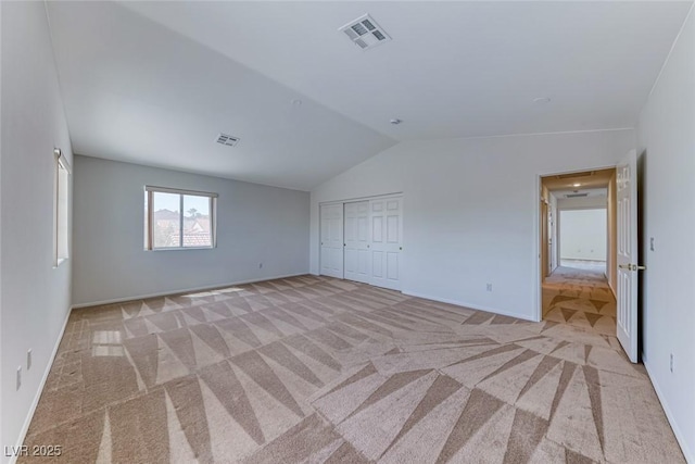 unfurnished bedroom featuring lofted ceiling, light carpet, baseboards, and a closet