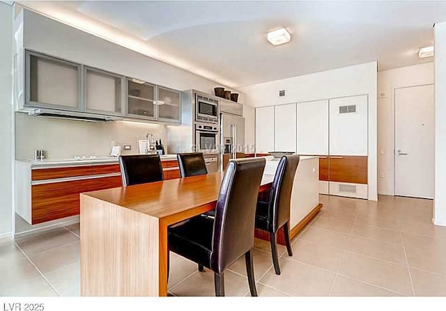 kitchen featuring appliances with stainless steel finishes, light tile patterned floors, glass insert cabinets, gray cabinetry, and light countertops