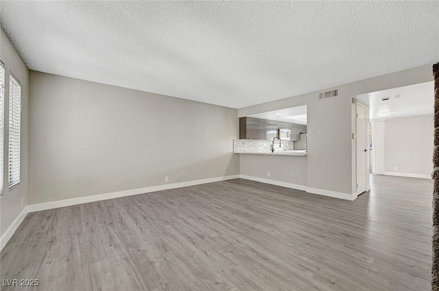 unfurnished living room featuring a textured ceiling, wood finished floors, and baseboards