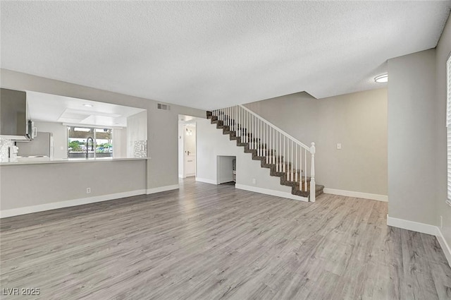 unfurnished living room featuring wood finished floors, a sink, a textured ceiling, stairway, and baseboards