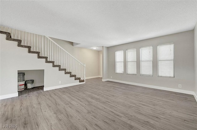 unfurnished living room featuring wood finished floors, a textured ceiling, stairs, and baseboards