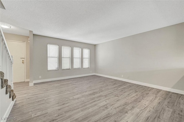 unfurnished living room with stairs, wood finished floors, a textured ceiling, and baseboards