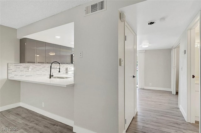 hall with light wood-style flooring, a sink, and baseboards