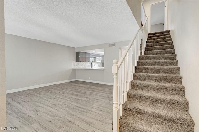 stairs with wood finished floors, a textured ceiling, and baseboards