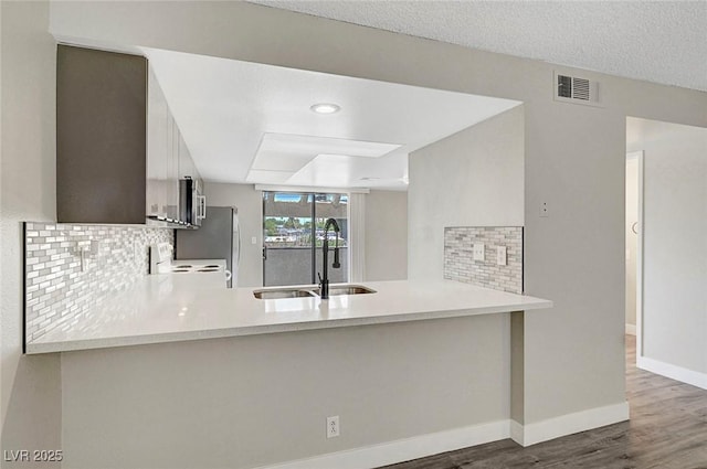 kitchen with a peninsula, backsplash, wood finished floors, white electric range, and baseboards