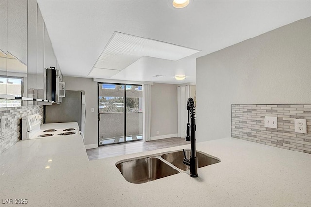 kitchen featuring white electric range oven, a sink, stainless steel microwave, light countertops, and decorative backsplash