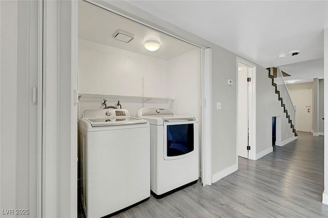 washroom featuring washing machine and dryer, light wood-type flooring, and baseboards