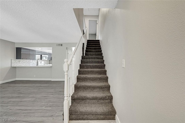 staircase with baseboards, a textured ceiling, and wood finished floors