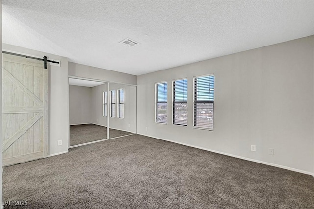 unfurnished bedroom with carpet, a barn door, baseboards, a textured ceiling, and a closet