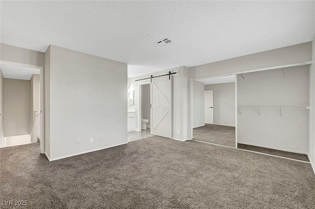 unfurnished bedroom featuring carpet flooring, a barn door, a textured ceiling, a closet, and connected bathroom