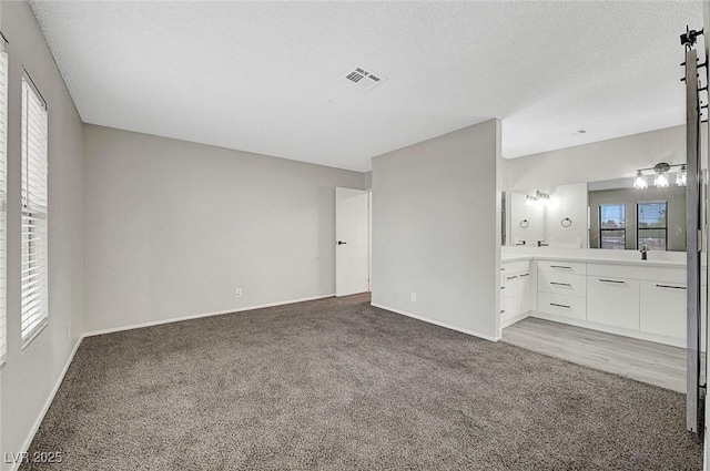 unfurnished bedroom featuring light colored carpet, baseboards, a textured ceiling, connected bathroom, and a sink