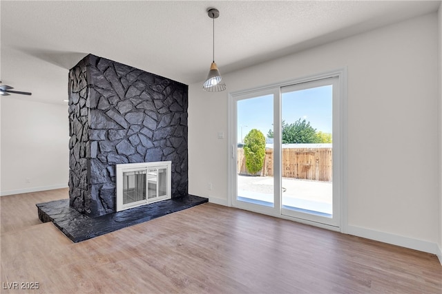 405 Oil Lantern Ln, Las Vegas, NV 89145 - unfurnished living room featuring wood finished floors, a stone fireplace, ceiling fan, baseboards, and a textured ceiling