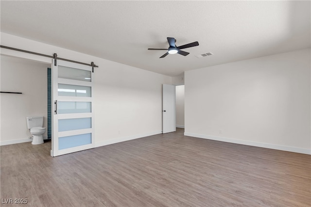 405 Oil Lantern Ln, Las Vegas, NV 89145 - unfurnished bedroom with a barn door, wood finished floors, baseboards, connected bathroom, and a ceiling fan