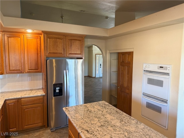 4455 W Ford Ave, Las Vegas, NV 89139 - kitchen featuring stainless steel fridge with ice dispenser, double oven, arched walkways, light stone counters, and brown cabinets