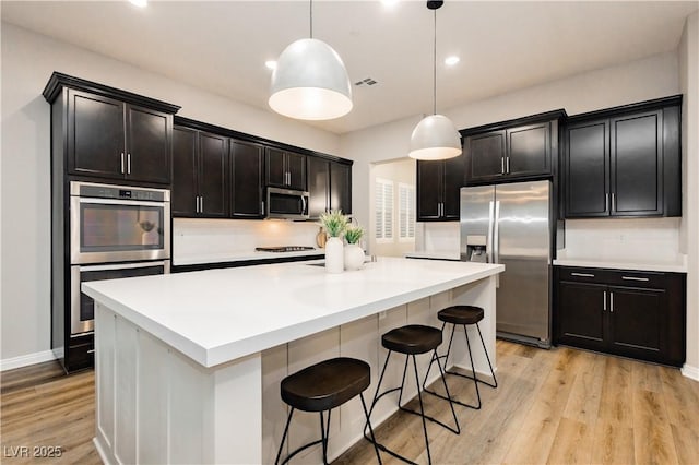 2450 Amatrice St, Henderson, NV 89044 - kitchen with appliances with stainless steel finishes, light wood-style flooring, a kitchen island with sink, decorative light fixtures, and baseboards