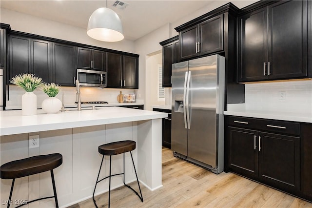 2450 Amatrice St, Henderson, NV 89044 - kitchen featuring stainless steel appliances, dark cabinets, backsplash, light wood-type flooring, and light countertops