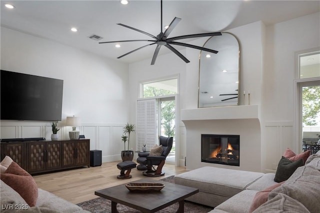 1610 Brock Ct, Las Vegas, NV 89117 - living room featuring a decorative wall, a ceiling fan, light wood-style floors, a wainscoted wall, and a glass covered fireplace