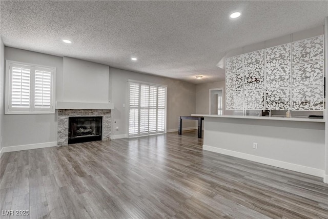 7905 Idledale Ct Unit 102, Las Vegas, NV 89145 - unfurnished living room with wood finished floors, a textured ceiling, baseboards, recessed lighting, and a glass covered fireplace
