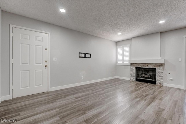 7905 Idledale Ct Unit 102, Las Vegas, NV 89145 - unfurnished living room featuring a textured ceiling, wood finished floors, recessed lighting, a stone fireplace, and baseboards