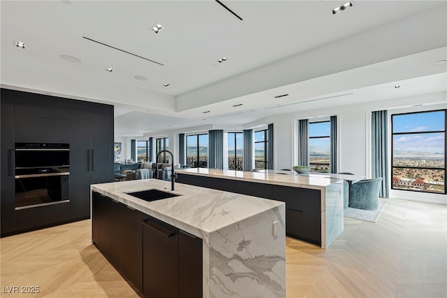 kitchen featuring modern cabinets, a sink, a large island, open floor plan, and light stone counters