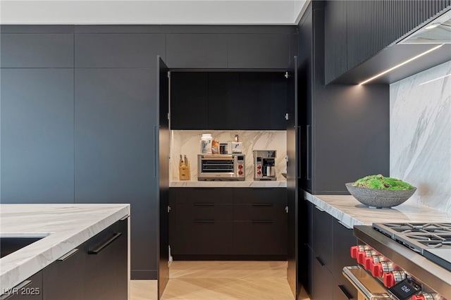 kitchen featuring high end range, modern cabinets, light stone counters, dark cabinets, and tasteful backsplash