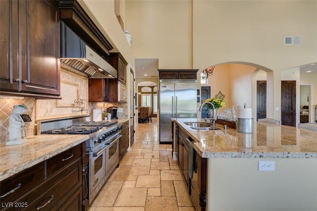 9749 Glistening Brook Ct, Las Vegas, NV 89149 - kitchen with built in appliances, a sink, arched walkways, a high ceiling, and stone tile flooring