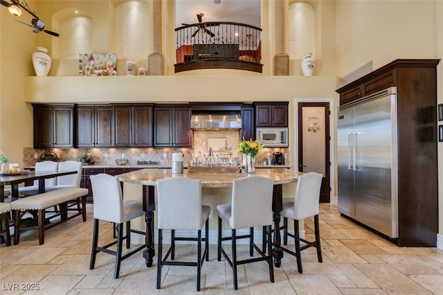 9749 Glistening Brook Ct, Las Vegas, NV 89149 - kitchen with built in appliances, stone tile floors, dark brown cabinets, and a towering ceiling