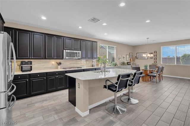 kitchen featuring stainless steel appliances, a sink, a breakfast bar area, backsplash, and light wood-type flooring