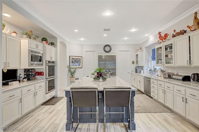729 Sir James Bridge Way, Las Vegas, NV 89145 - kitchen with built in appliances, white cabinetry, glass insert cabinets, light wood-style flooring, and crown molding