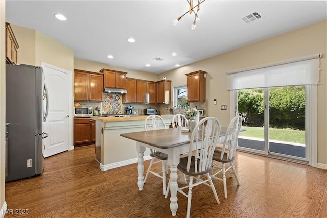 6049 Paddleboat St, North Las Vegas, NV 89031 - kitchen with appliances with stainless steel finishes, wood finished floors, brown cabinets, under cabinet range hood, and backsplash